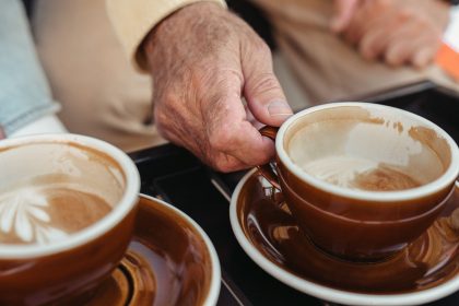 A senior adult's hand holding a brown coffee cup in an intimate cafe setting.