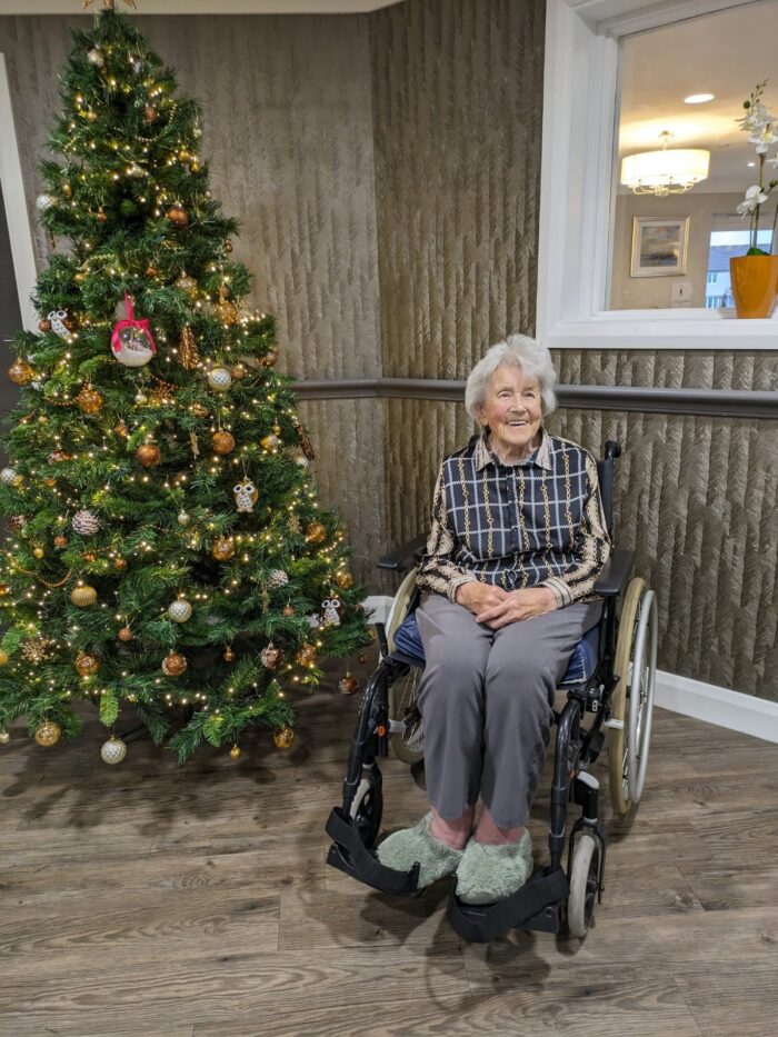 Resident at Avocet House smiling beside a beautifully decorated Christmas tree during the festive season.