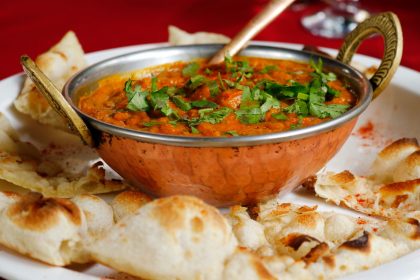 Indian curry garnished with coriander served with naan in a copper dish.
