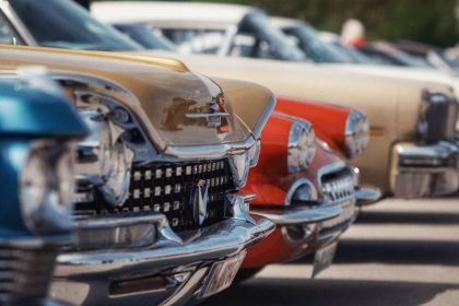 Colorful vintage cars lined up in perfect alignment at an outdoor car show under a clear sky.
