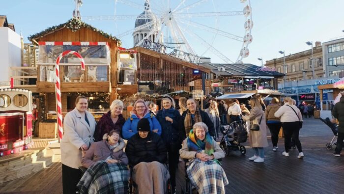 Beeston Rise residents and team members enjoying a festive visit to Nottingham Winter Wonderland, gathered in front of the Christmas market and Ferris wheel.