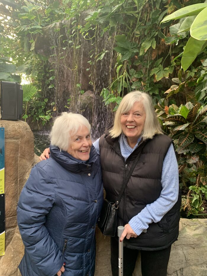 Two Bingley Park residents smiling during a visit to Tropical World, standing in front of a lush indoor waterfall.