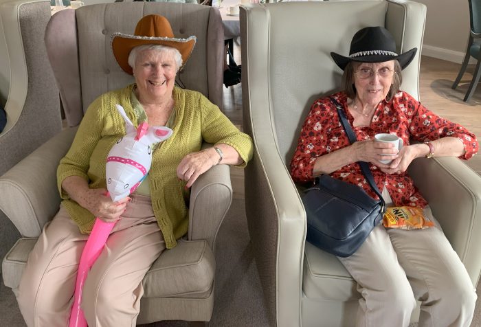 Two Avocet House residents wearing cowboy hats and smiling during a Wild West-themed activity, with one holding a hobby horse.