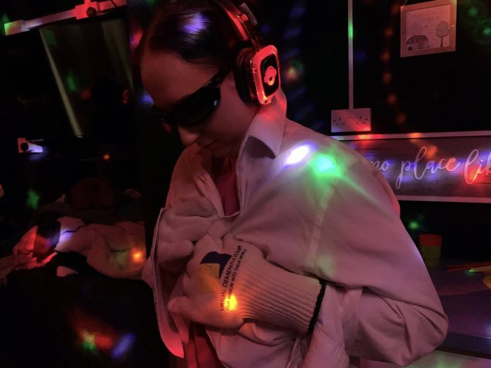Resident enjoys a sensory experience with headphones, protective glasses and coloured lights during an immersive activity session at a care home.