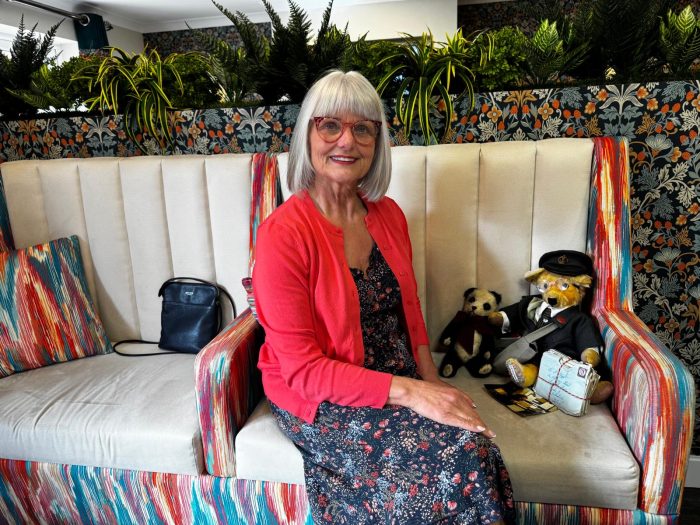 Dawn Argyle sitting on a colourful sofa at York Manor Care Home next to two restored vintage teddy bears, including Frank the postman bear.