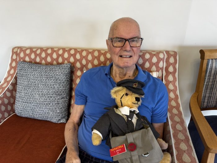 88-year-old York Manor resident Frank Argyle smiling on a sofa while holding the restored postman teddy bear.
