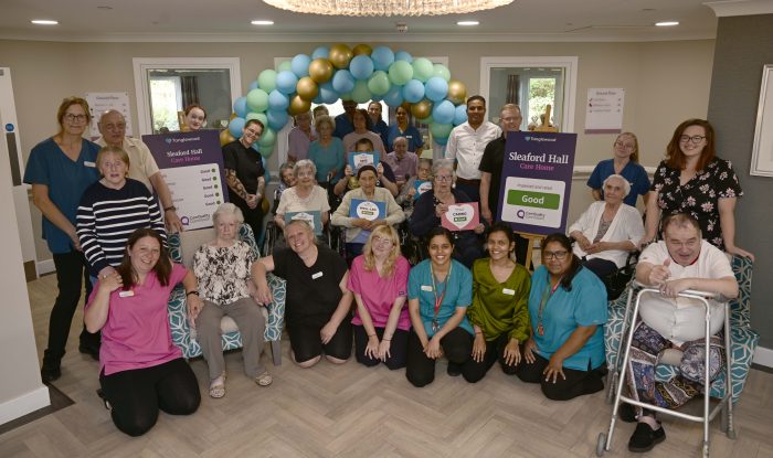 A group of staff at Sleaford Hall Care Home cheering and waving outside while holding CQC Good rating placards and category signs.