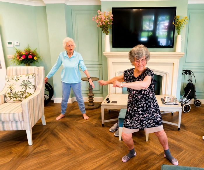 Former professional dance teacher Sylvia Hawley demonstrating a dance routine in the lounge at Gateford Lodge with another resident following along behind her.