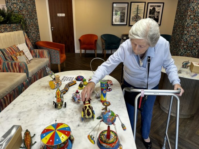 86-year-old resident Mary Robinson using a walking frame while examining colourful vintage tin toys during a reminiscence therapy activity at York Manor.